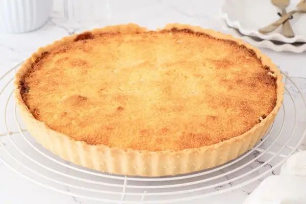 Tarta de coco dorada y crujiente sobre una rejilla. Su relleno esponjoso y aroma tropical invitan a probar esta delicia.