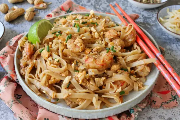 Un delicioso plato de pad thai con camarones, fideos de arroz, cacahuetes picados y cebollino.