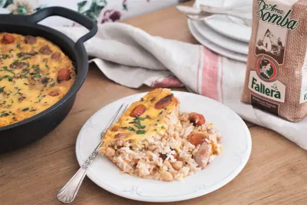 Un delicioso arroz con costra recién hecho, con trozos de salchicha y garbanzos, servido en un plato blanco.