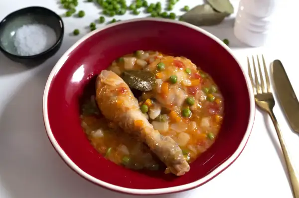 Un delicioso pollo a la jardinera en un cuenco rojo, con guisantes, zanahoria y laurel.