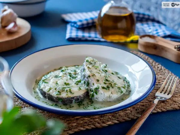 Dos rodajas de merluza en salsa verde, con perejil picado y una cremosa salsa. Un plato casero listo para disfrutar.