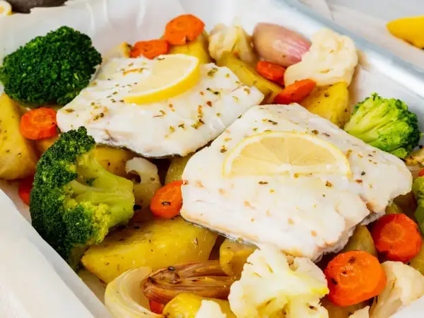 Bacalao al horno con patatas, brócoli, zanahorias y coliflor, todo asado en una bandeja.