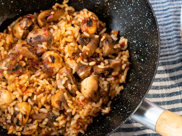 Arroz con champiñones recién hecho en sartén, con trozos dorados de champiñones y un toque de pimiento rojo.