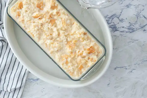 Preparando una deliciosa receta de pudin casero en un molde de vidrio, con trozos de galleta integrados.