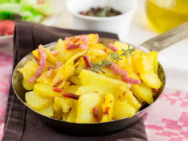 Patatas al microondas con trocitos de bacon crujiente y romero fresco, servidas en una sartén metálica. ¡Un plato sencillo y delicioso!