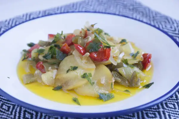 Patatas a lo pobre con pimientos rojos y verdes, cebolla y perejil, servidas en un plato blanco con borde azul.