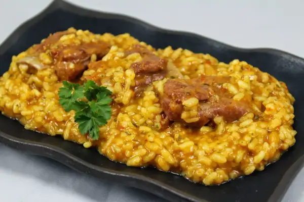 Arroz con costillas jugosas, preparado en Thermomix, servido en plato negro con perejil fresco.