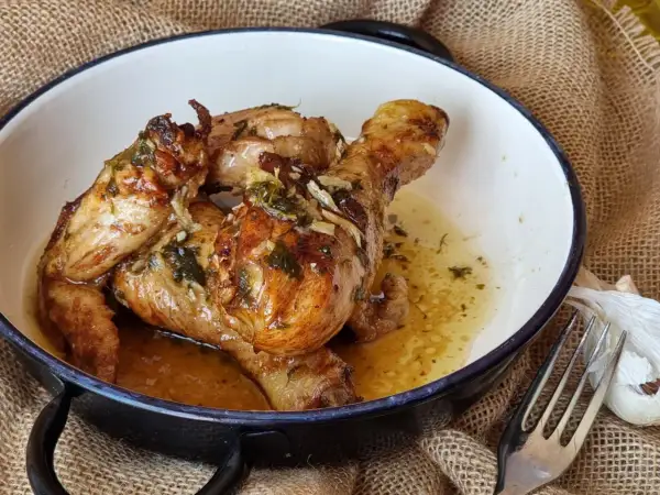 Sabroso pollo al ajillo dorado y jugoso, bañado en su propio jugo con ajo y hierbas, servido en una cazuela.