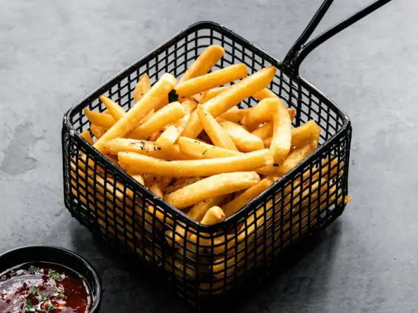 Cesta negra llena de crujientes patatas fritas doradas, listas para ser disfrutadas con una salsa roja.