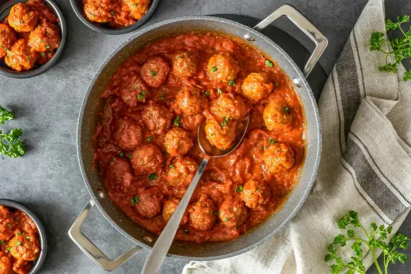 Sabrosas almondigas en salsa roja, recién servidas en una sartén, con perejil fresco espolvoreado. ¡Un plato casero irresistible!