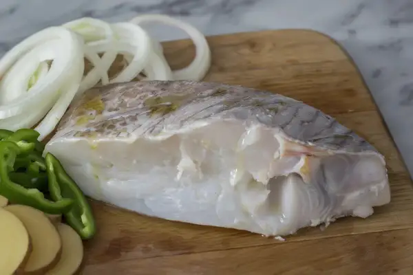Filete de bacalao fresco con rodajas de patata, pimiento verde y cebolla, listo para preparar deliciosas recetas de bacalao.