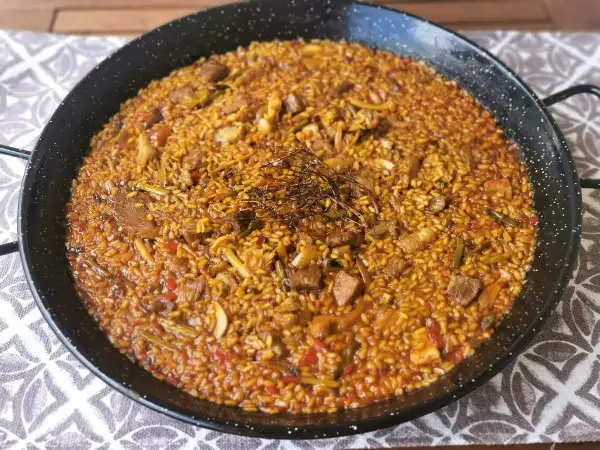 Arroz con secreto, un plato de paella con trozos de carne, pimientos y judías verdes, coronado con hierbas aromáticas.