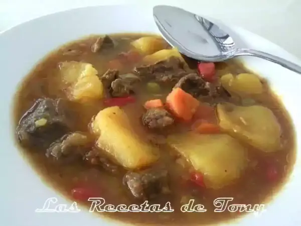 Un plato humeante de patatas con carne olla express, con trozos de zanahoria y pimiento rojo.