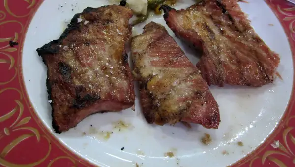 Tres jugosas porciones de secreto ibérico a la parrilla, con sal gruesa y un toque de pimienta, servidas en un plato blanco con borde rojo.