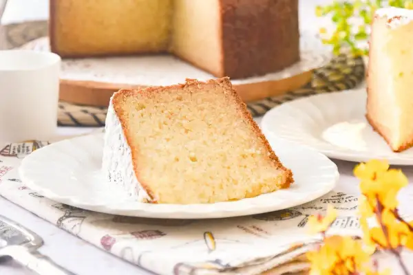 Rebanada de bizcocho de leche caliente, esponjoso y espolvoreado con azúcar glas, servido en plato blanco.