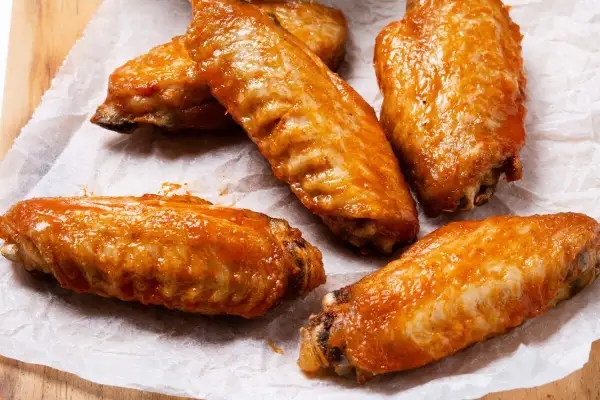 Cinco alitas de pollo al horno crujientes, cubiertas con una salsa brillante y apetitosa, listas para disfrutar.
