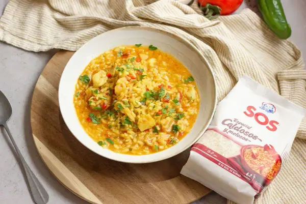 Un plato de arroz con bacalao, pimientos y perejil, acompañado de un paquete de arroz SOS especial caldosos.