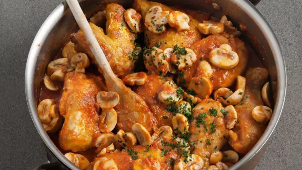 Pollo con gambas y champiñones en salsa roja, servido en una olla de metal con una cuchara de madera.