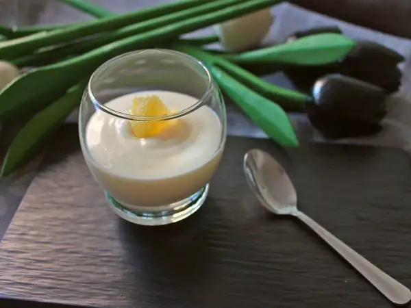 Delicioso postre de lemon curd en copa, decorado con un trozo de limón. Una cuchara plateada y tulipanes negros completan la escena.