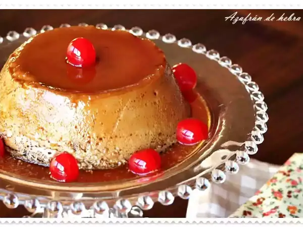 Delicioso flan de café con caramelo líquido y cerezas rojas, servido en un plato de cristal decorado.