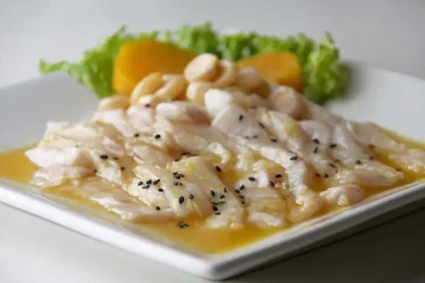 Delicioso tiradito de corvina fresco, bañado en una salsa cítrica y adornado con semillas de sésamo negro, acompañado de camote y lechuga.