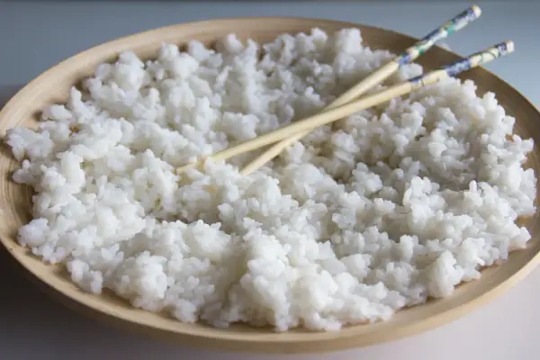 Arroz para sushi listo para preparar tus makis favoritos. Palillos cruzados sobre el arroz blanco y pegajoso en un cuenco de madera.